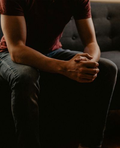 Person sitting with clasped hands on lap, representing reflection and support in individual therapy sessions